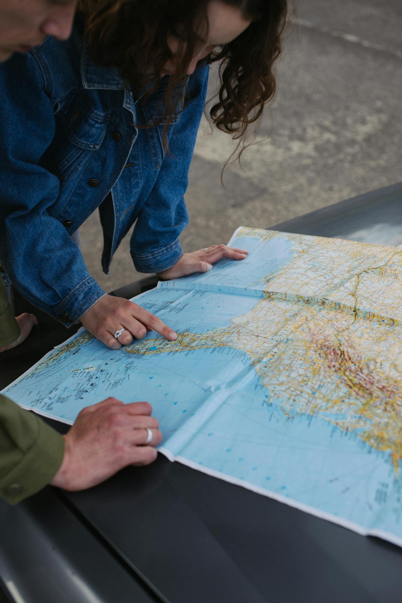 A couple examines a map on a car's hood, planning their travel route.