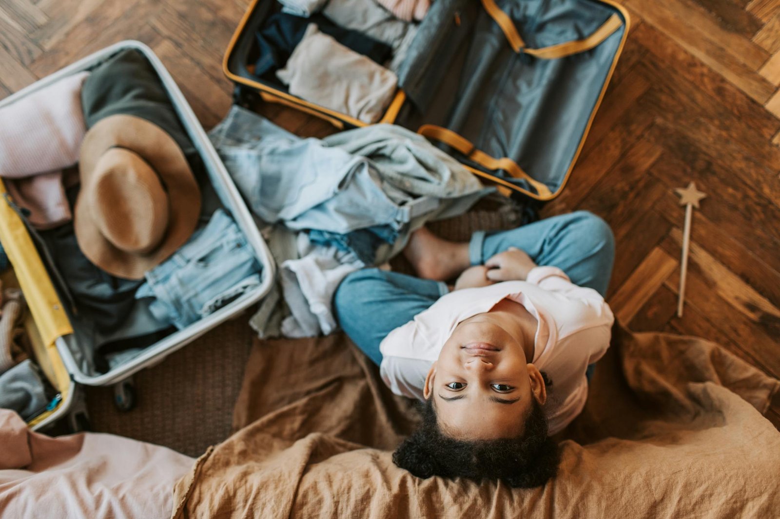Young child surrounded by clothes and an open suitcase, preparing for a trip indoors.